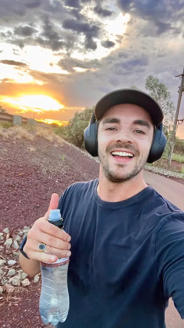 Paul, lachend met pet en koptelefoon bij zonsondergang