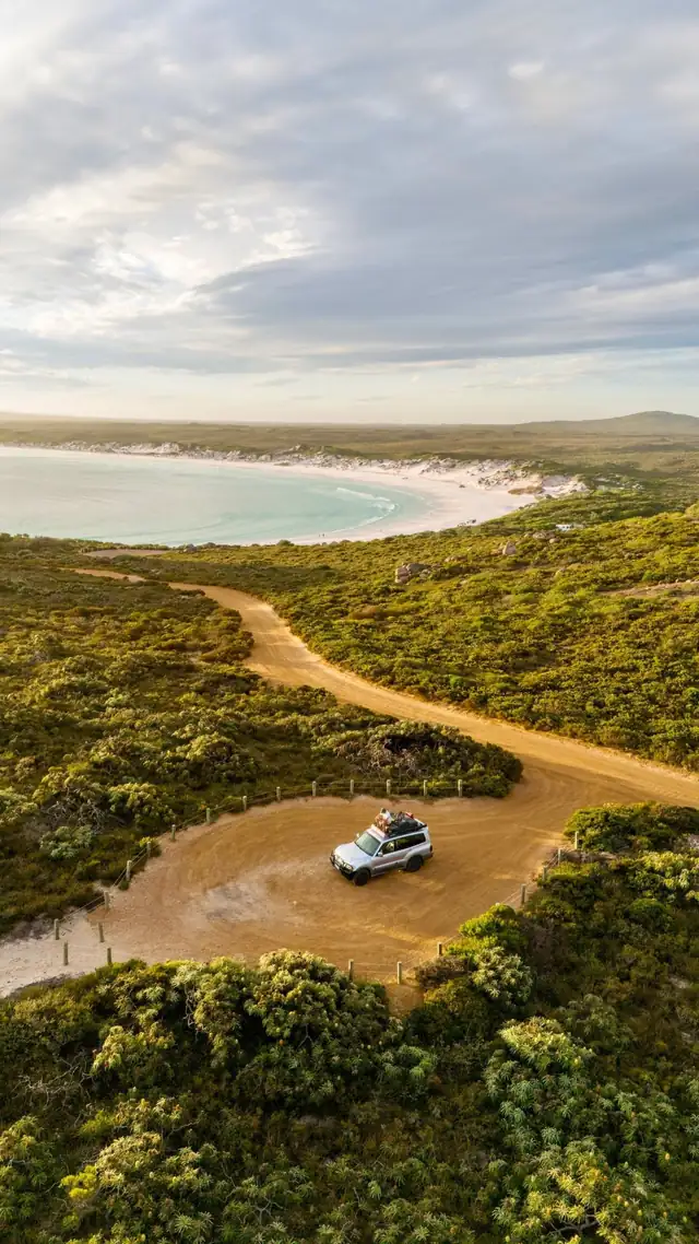 Drone-shot van een auto op een zandweg boven een witte baai in West-Australië
